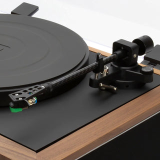 Close-up of a turntable with a black vinyl record, black plinth, wood-grain outer body, and a black tonearm with a gold and silver cartridge.
