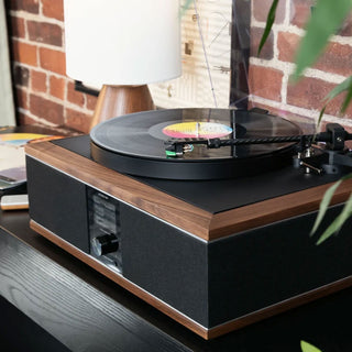 Turntable with a vinyl record on a wooden turntable stand against a brick wall.