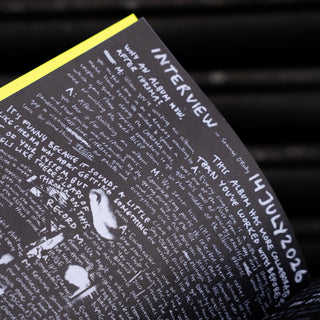 A close-up angled shot of an open printed booklet or magazine page with dense white text on a black background and a bright yellow page edge, set against a dark blurred background.