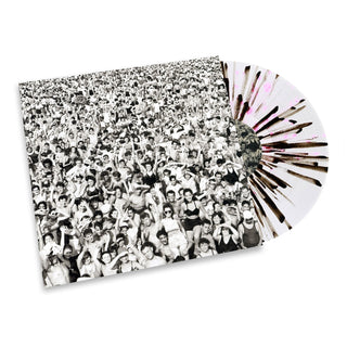 A vinyl record partially slid out of its sleeve, with the sleeve printed in black and white photography of a large crowd and the record itself featuring a white base with black radial streaks and a few pink splatters.