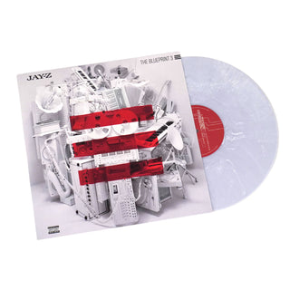 A vinyl record album shown at an angle with the sleeve on the left and the translucent record partially visible on the right. The sleeve features a white collage of electronic devices and objects with bold red horizontal bands, and the record itself is pale translucent white with a red center label.