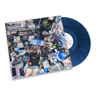 A vinyl record partially pulled from its sleeve, showing a dark blue record and a highly detailed collage cover with electronics, screens, and a person in a cluttered room scene, on a white background.
