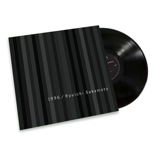 A vinyl record partially pulled from its sleeve, showing a black striped album cover with white text reading '1996 / Ryuichi Sakamoto' on a clean white background.