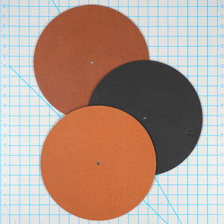 Three circular textured material samples in terracotta orange, black, and a lighter orange, arranged overlapping on a blue grid background.